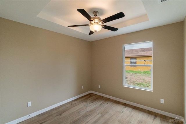 empty room featuring ceiling fan, light hardwood / wood-style floors, and a tray ceiling