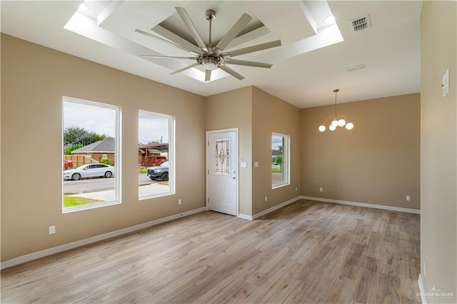 empty room featuring ceiling fan with notable chandelier, a healthy amount of sunlight, and light hardwood / wood-style flooring