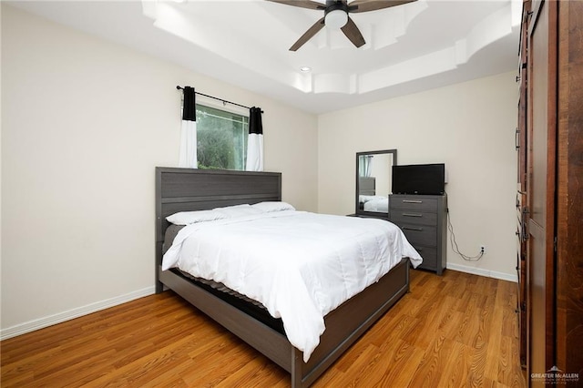 bedroom with a raised ceiling, ceiling fan, and light wood-type flooring