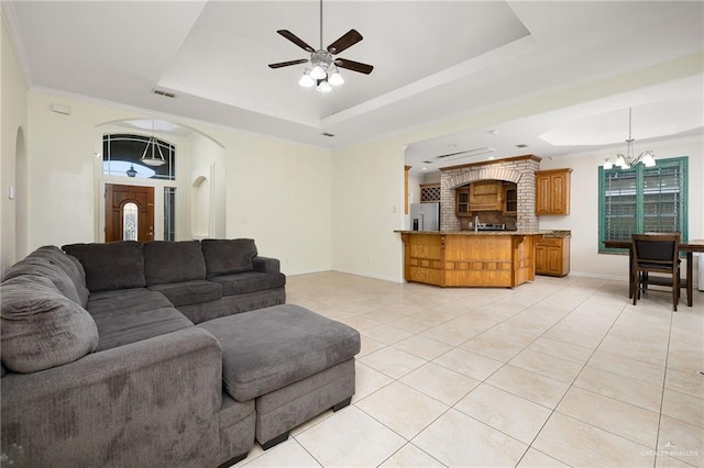 tiled living room with ceiling fan with notable chandelier, ornamental molding, and a tray ceiling