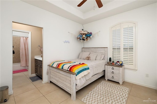 tiled bedroom featuring ceiling fan, ensuite bath, and a tray ceiling