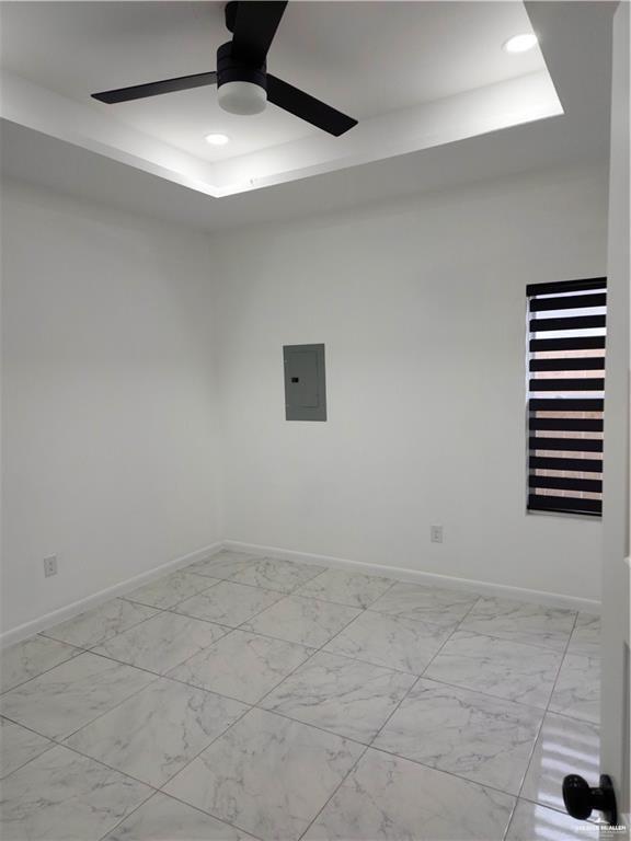 empty room featuring ceiling fan, electric panel, and a raised ceiling