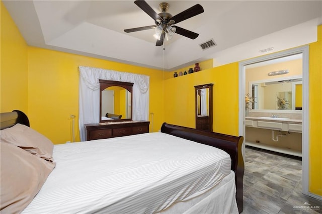 bedroom featuring a tray ceiling, connected bathroom, ceiling fan, and sink