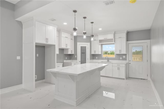 kitchen with a kitchen island, pendant lighting, sink, white cabinets, and light stone counters