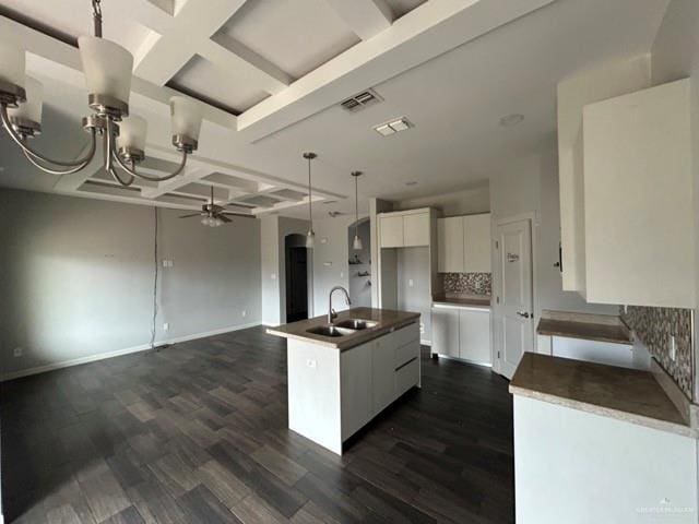 kitchen featuring coffered ceiling, sink, white cabinetry, a center island with sink, and ceiling fan