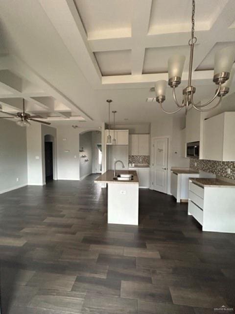 kitchen featuring sink, white cabinetry, hanging light fixtures, coffered ceiling, and an island with sink