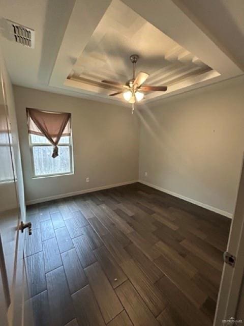 spare room featuring a tray ceiling, dark wood-type flooring, and ceiling fan