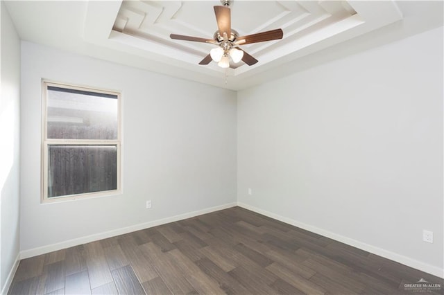 empty room featuring a tray ceiling, dark wood-type flooring, and ceiling fan