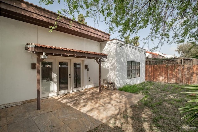 rear view of house featuring french doors, a patio area, fence, and stucco siding