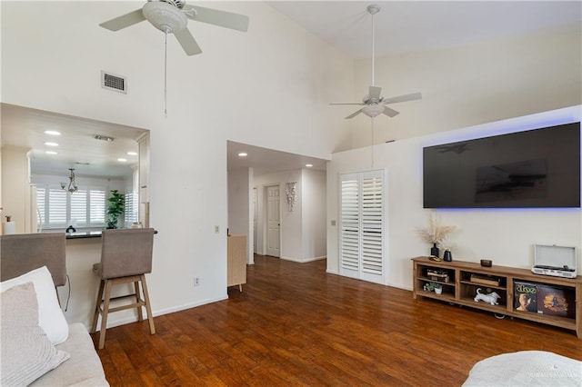 living area with a ceiling fan, visible vents, a towering ceiling, and wood finished floors