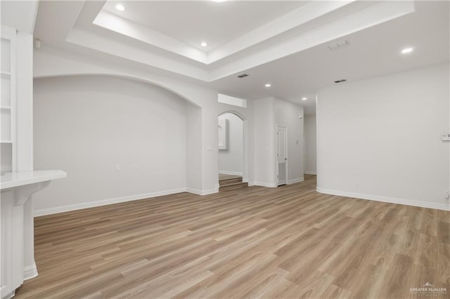 unfurnished living room with light wood-type flooring and a tray ceiling