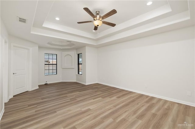 spare room with ceiling fan, light hardwood / wood-style flooring, and a tray ceiling