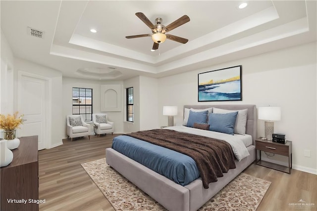 bedroom featuring a raised ceiling, wood-type flooring, and ceiling fan