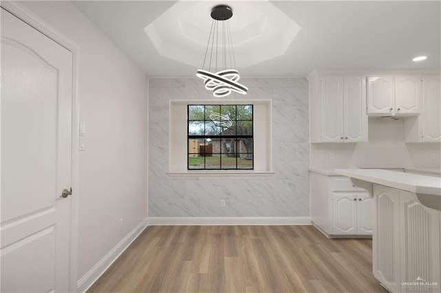 unfurnished dining area with an inviting chandelier, light hardwood / wood-style floors, and a raised ceiling