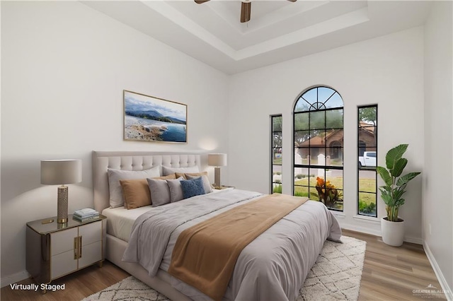 bedroom with ceiling fan, light wood-type flooring, and a tray ceiling