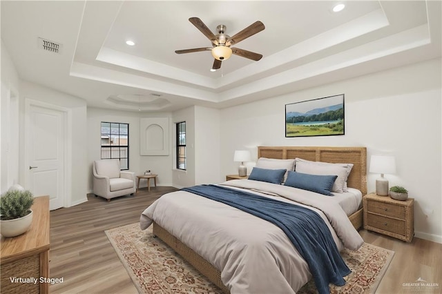 bedroom with ceiling fan, light wood-type flooring, and a tray ceiling