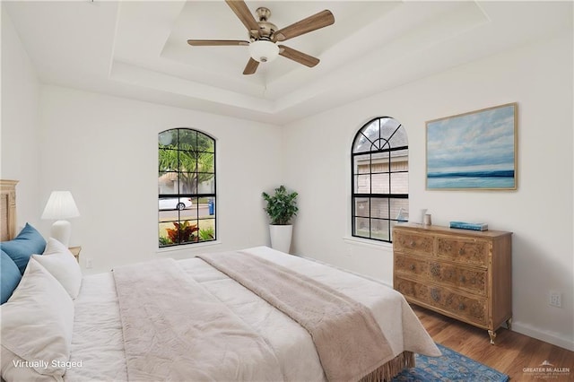 bedroom with ceiling fan, multiple windows, a raised ceiling, and hardwood / wood-style floors