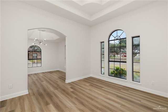 empty room with hardwood / wood-style floors, a tray ceiling, and a notable chandelier