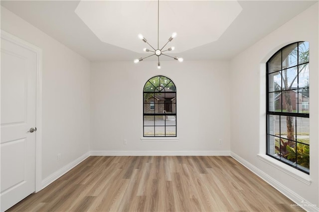 empty room with light wood-type flooring, a healthy amount of sunlight, and an inviting chandelier