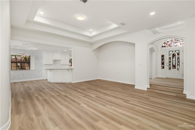 unfurnished living room featuring light wood-type flooring, plenty of natural light, and a tray ceiling