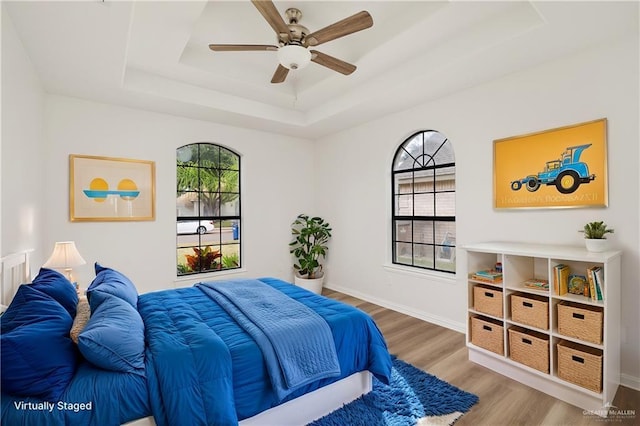 bedroom with ceiling fan, multiple windows, wood-type flooring, and a raised ceiling