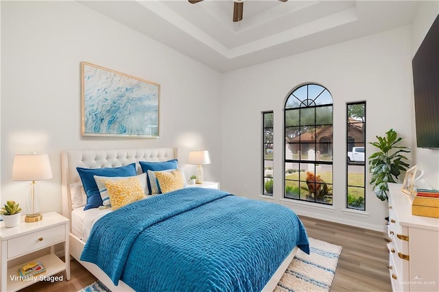 bedroom featuring ceiling fan, a raised ceiling, hardwood / wood-style flooring, and multiple windows