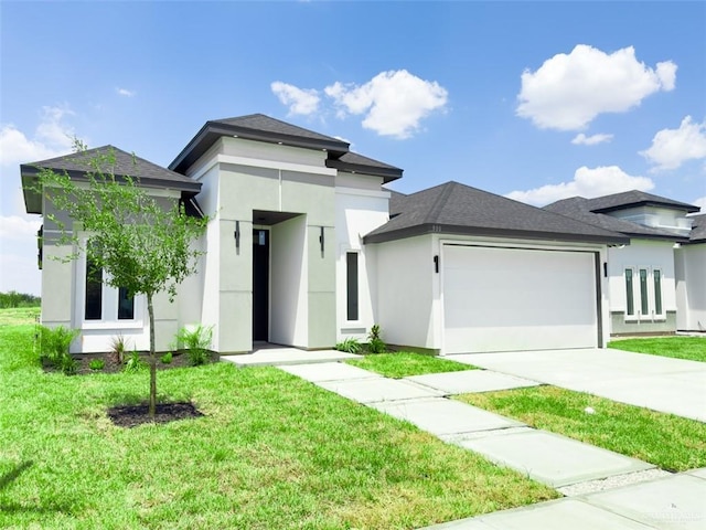 prairie-style home with an attached garage, a shingled roof, concrete driveway, stucco siding, and a front lawn