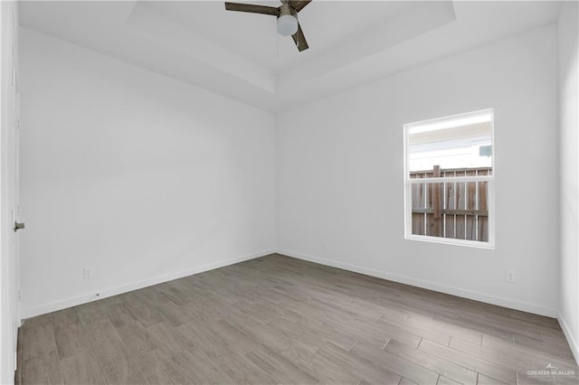 spare room with light hardwood / wood-style floors, a raised ceiling, and ceiling fan