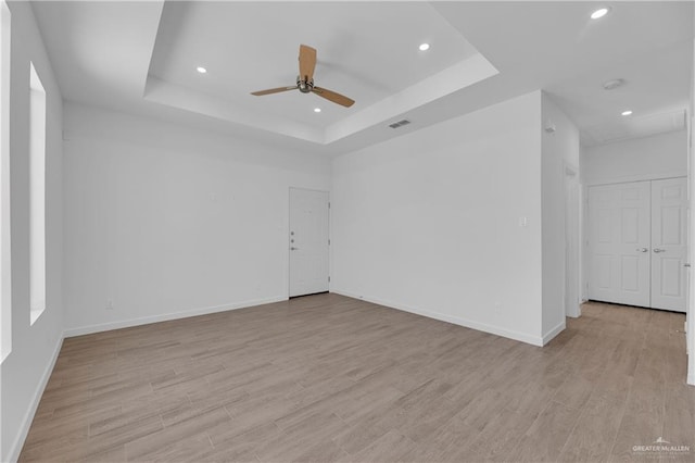 empty room with light hardwood / wood-style floors, a raised ceiling, and ceiling fan