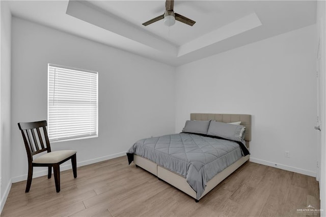 bedroom featuring light hardwood / wood-style flooring, a raised ceiling, and ceiling fan