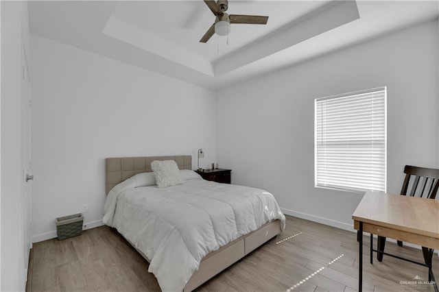 bedroom featuring ceiling fan, light wood-type flooring, and a tray ceiling