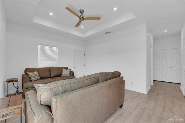 living room featuring a raised ceiling, ceiling fan, and light wood-type flooring