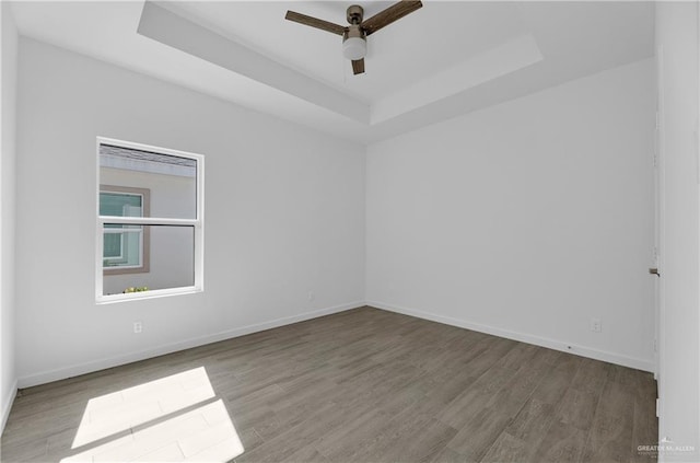 empty room with ceiling fan, a tray ceiling, and light hardwood / wood-style flooring