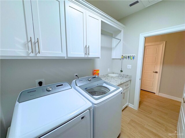 laundry room featuring washer and dryer, cabinets, and light hardwood / wood-style flooring