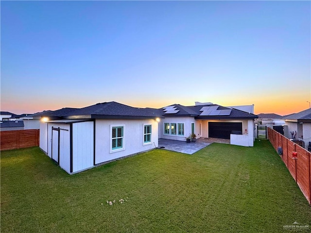 back house at dusk with a lawn, solar panels, and a patio area