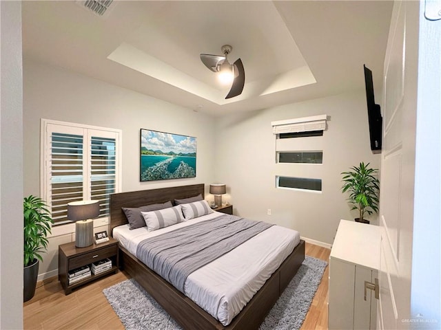 bedroom featuring a tray ceiling, ceiling fan, and light wood-type flooring