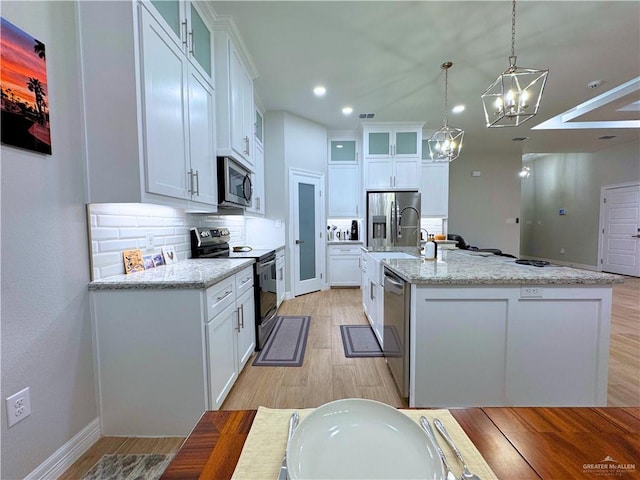 kitchen featuring white cabinets, appliances with stainless steel finishes, pendant lighting, and an island with sink