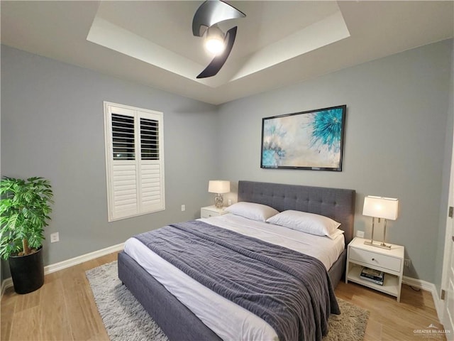 bedroom featuring ceiling fan, light hardwood / wood-style floors, and a tray ceiling