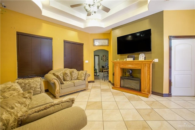 tiled living room with a raised ceiling and ceiling fan