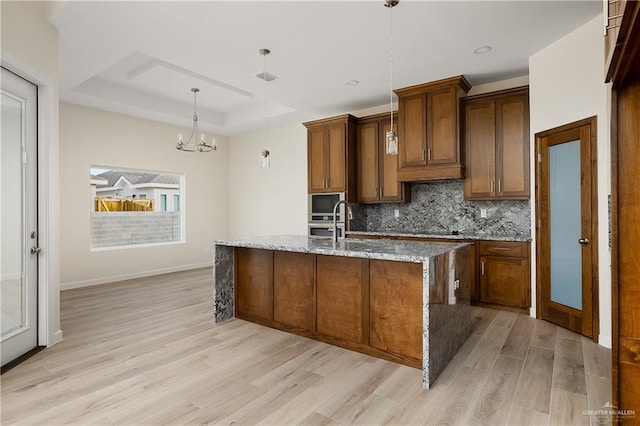 820 N Brushfield Ave, Edinburg, TX 78541 - kitchen featuring light wood finished floors, a raised ceiling, decorative backsplash, light stone countertops, and an island with sink