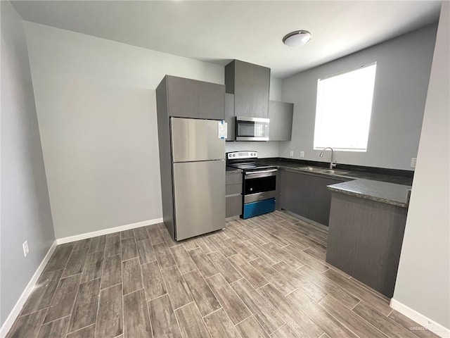 kitchen with stainless steel appliances, a sink, baseboards, wood tiled floor, and dark countertops