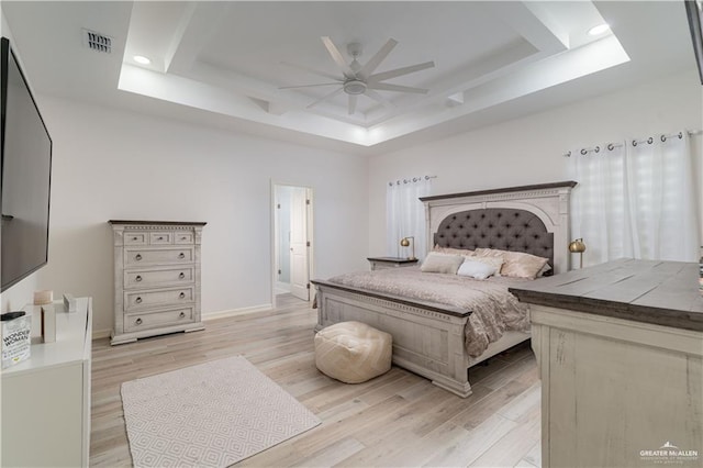 bedroom with ceiling fan, a tray ceiling, and light hardwood / wood-style flooring