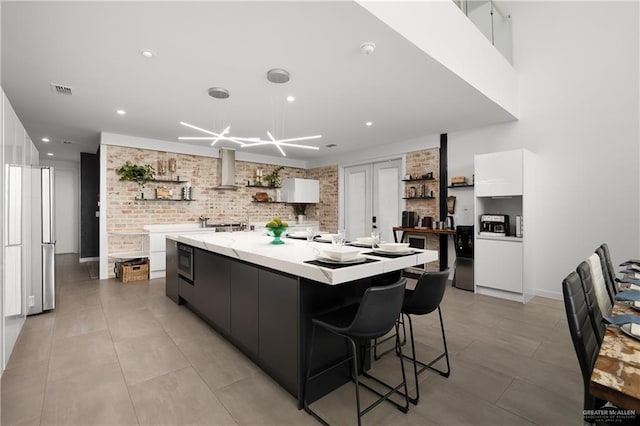 kitchen featuring exhaust hood, brick wall, white cabinets, pendant lighting, and a spacious island