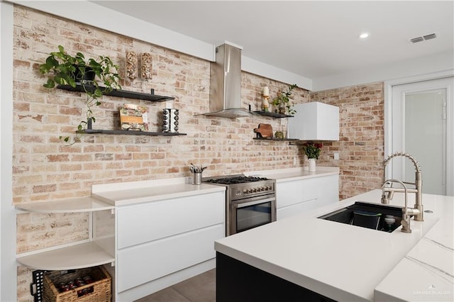 kitchen with sink, wall chimney range hood, white cabinets, and high end stainless steel range