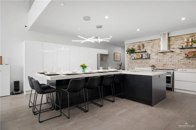 kitchen with high end stainless steel range oven, white cabinetry, an island with sink, and wall chimney range hood