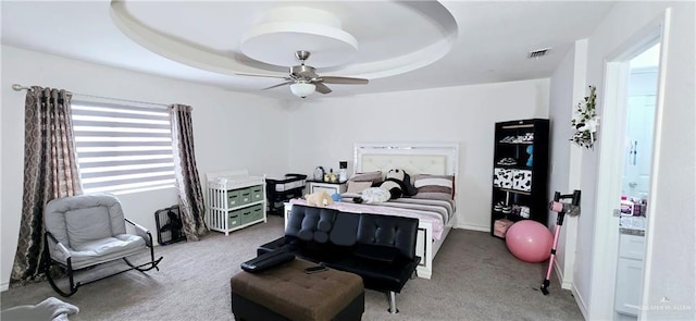 bedroom featuring light carpet, visible vents, a raised ceiling, and a ceiling fan