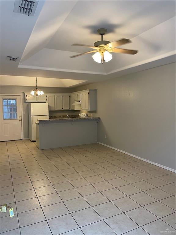 kitchen featuring a tray ceiling, freestanding refrigerator, visible vents, and a peninsula