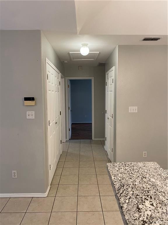 corridor featuring baseboards, visible vents, and light tile patterned flooring