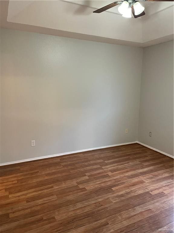 unfurnished room featuring dark wood-type flooring, a ceiling fan, and baseboards