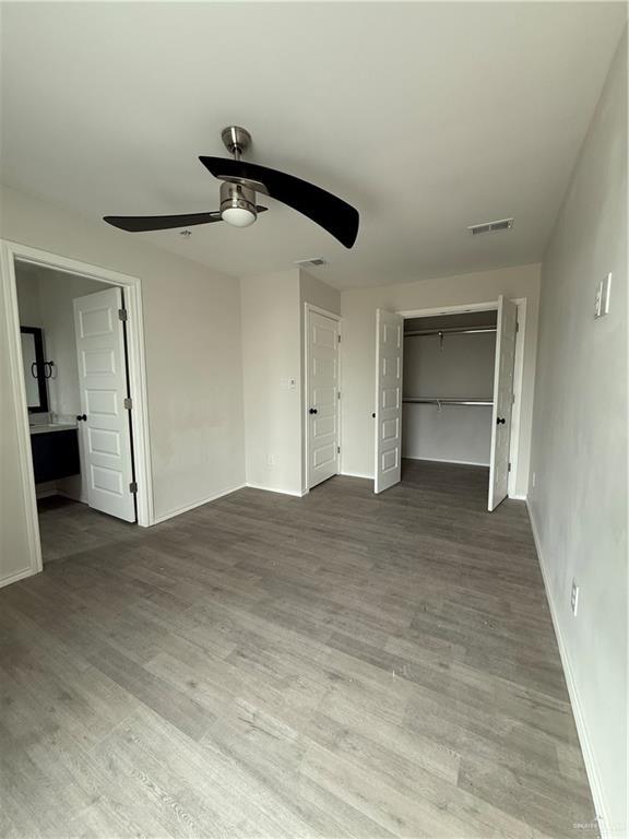 unfurnished bedroom with ensuite bath, ceiling fan, a closet, and wood-type flooring